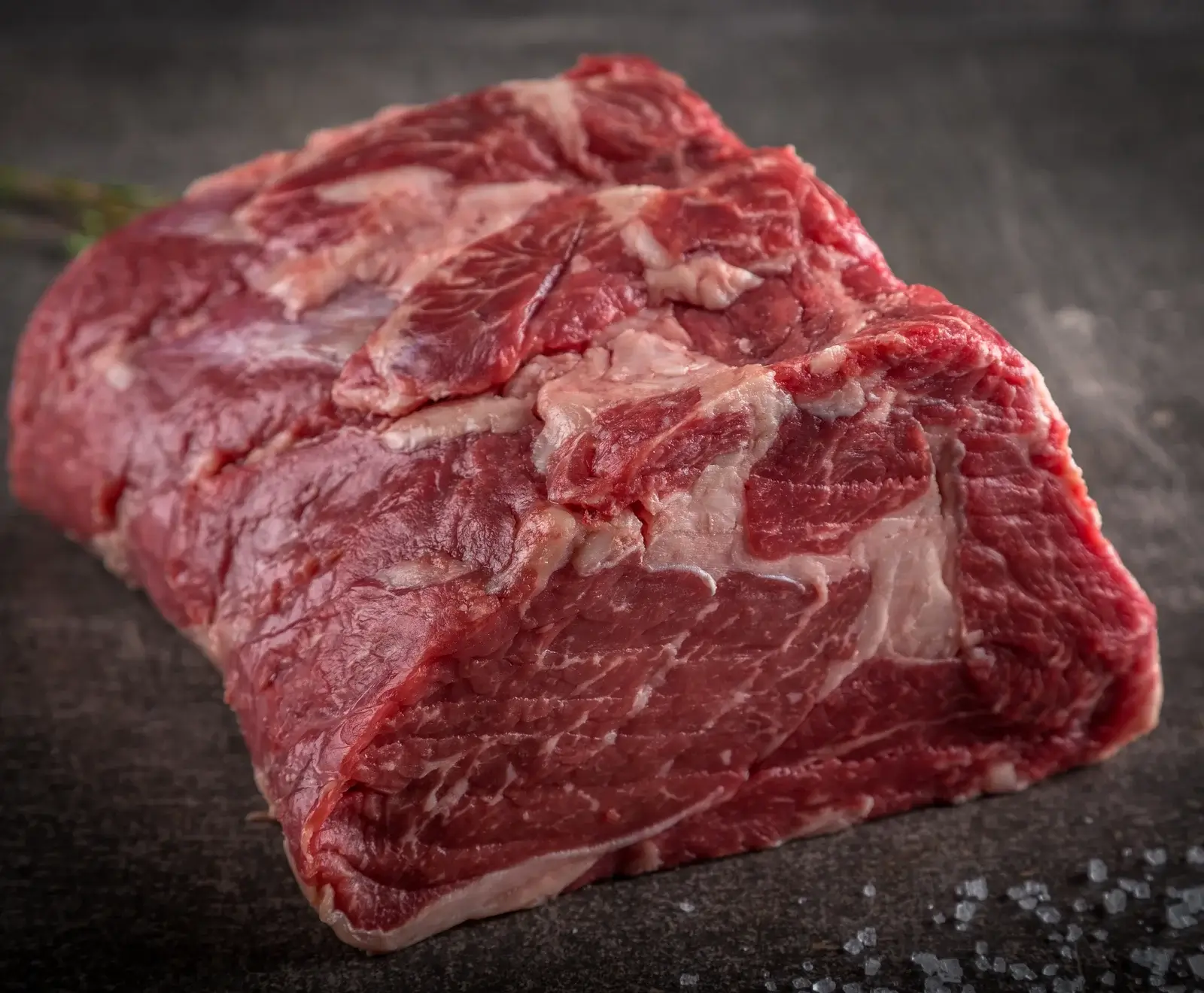 Rohes Rindersteak mit sichtbarem Fettmarmor auf dunklem Hintergrund mit Salz bestreut