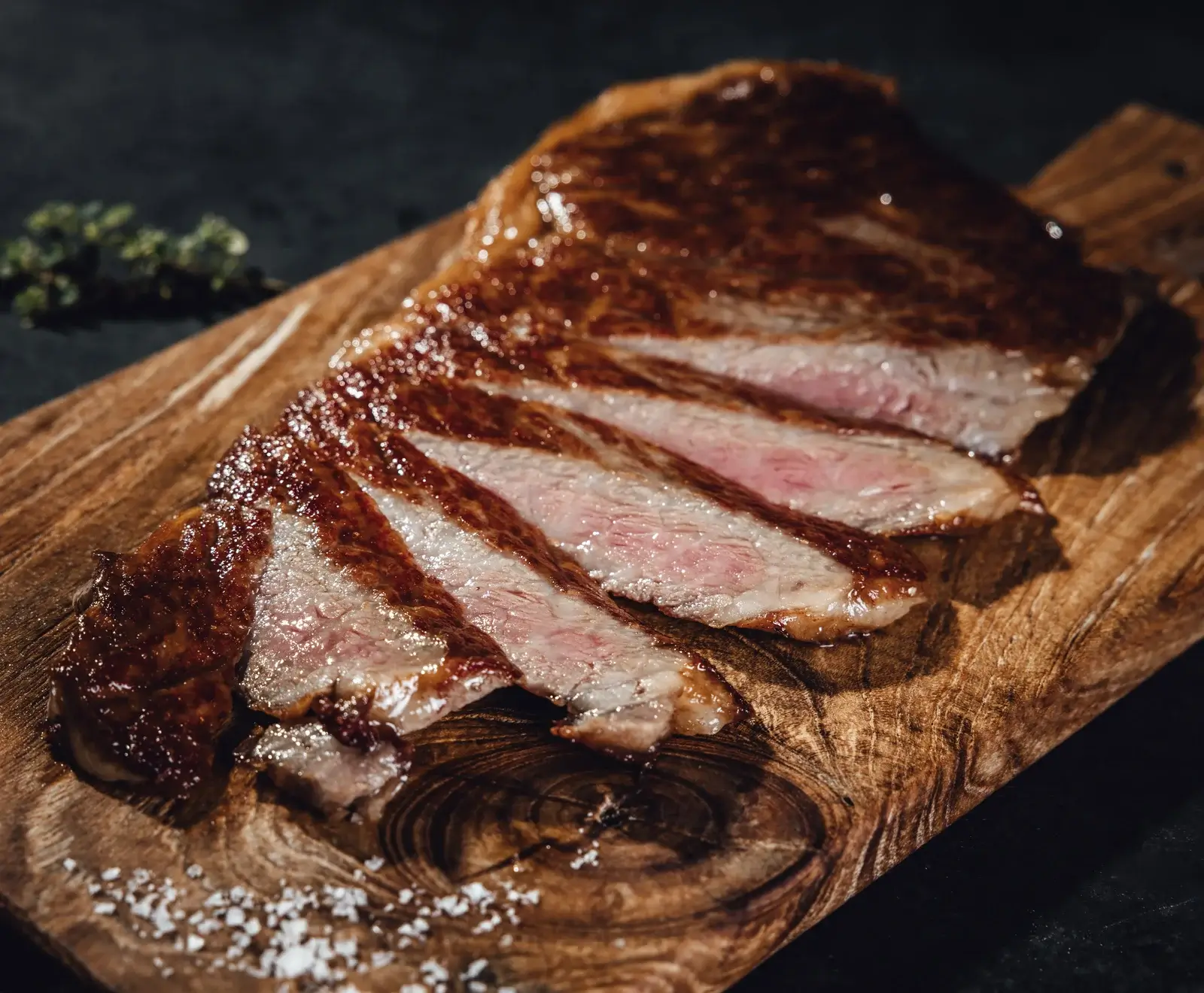 Ein saftiges, in Scheiben geschnittenes Steak, medium-rare gebraten, mit knuspriger Kruste, auf einem rustikalen Holzbrett mit grobem Meersalz und Kräutern.