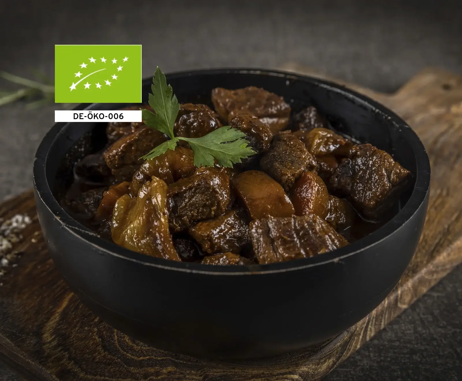 Schüssel mit gekochtem Rindfleisch in dunkler Soße, garniert mit Petersilie, auf Holzuntergrund