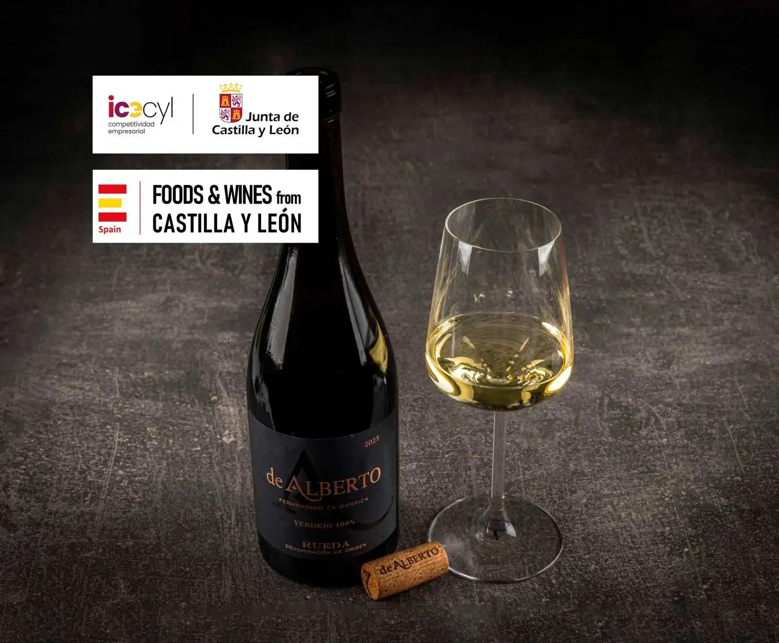 Flasche De Alberto Verdejo Weißwein (Rueda D.O.) und ein gefülltes Weinglas auf dunklem Untergrund. Oben links Logos von Junta de Castilla y León und Foods & Wines from Castilla y León.