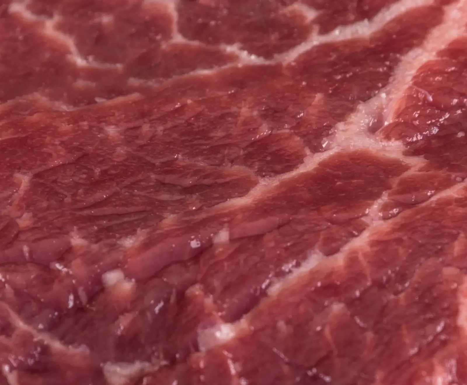 Nahaufnahme von rohem, dunkelrotem Fleisch mit deutlicher weißer Marmorierung und faseriger Textur.