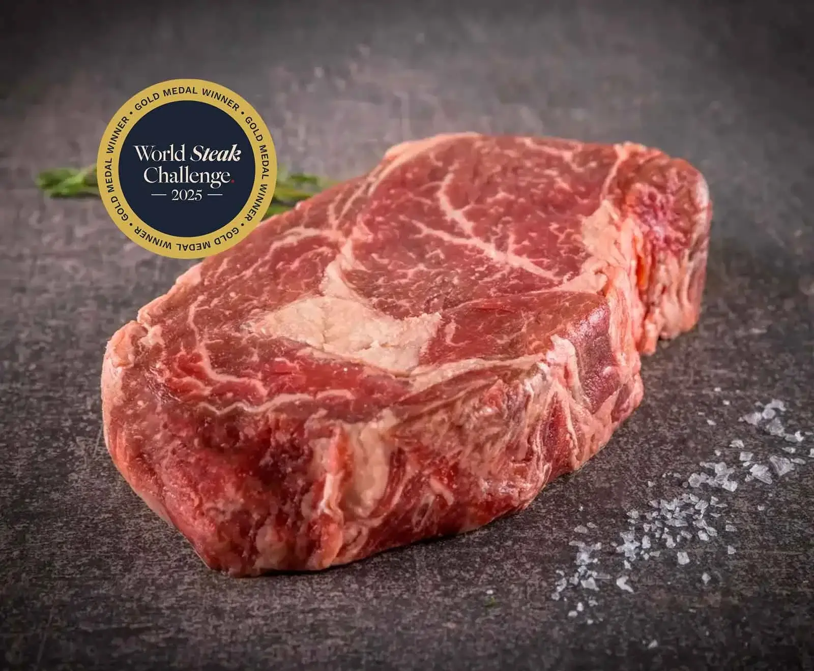 Rohes, gut marmoriertes Ribeye-Steak auf dunklem Untergrund mit Meersalz. Ein goldenes Abzeichen "World Steak Challenge 2025 Gold Medal Winner" ist oben links eingeblendet.