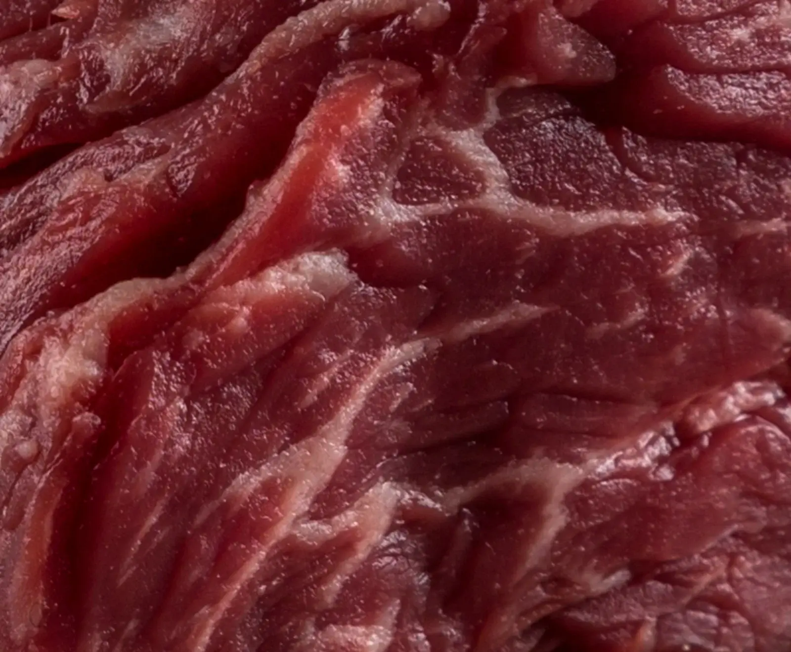 Nahaufnahme von rotem, rohem Fleisch mit deutlicher Marmorierung und feinen Fettstreifen, die sich durch das Muskelfleisch ziehen.