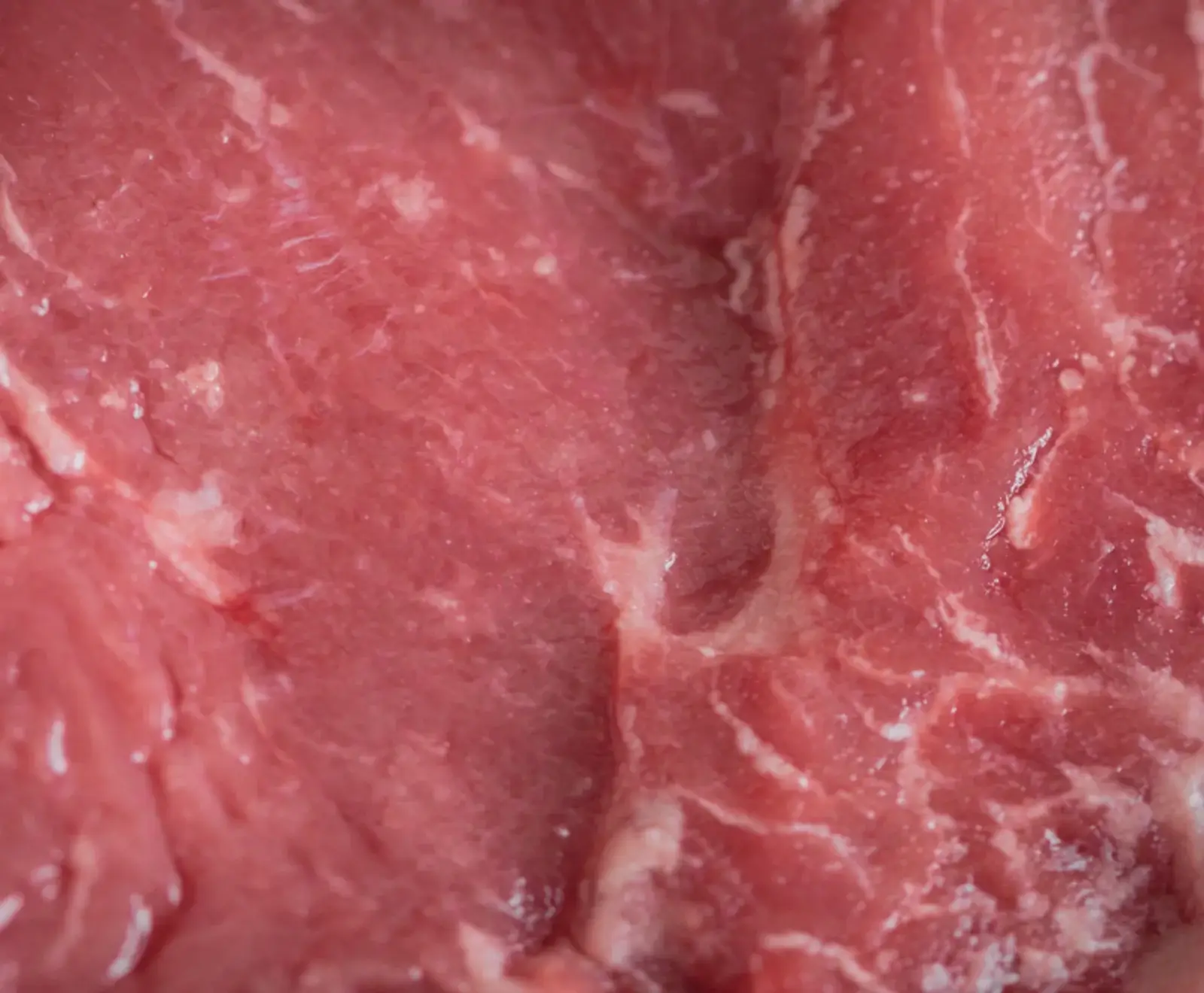 Makroaufnahme von frischem, rotem Fleisch, das Muskelfasern und feine weiße Fettmarmorierung zeigt. Die Oberfläche ist leicht glänzend und feucht.
